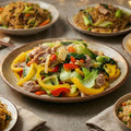 Plates of Mai-o-Mailee's Mom's All Purpose Seasoning stir-fried vegetables and meat with noodles on a wooden table.
